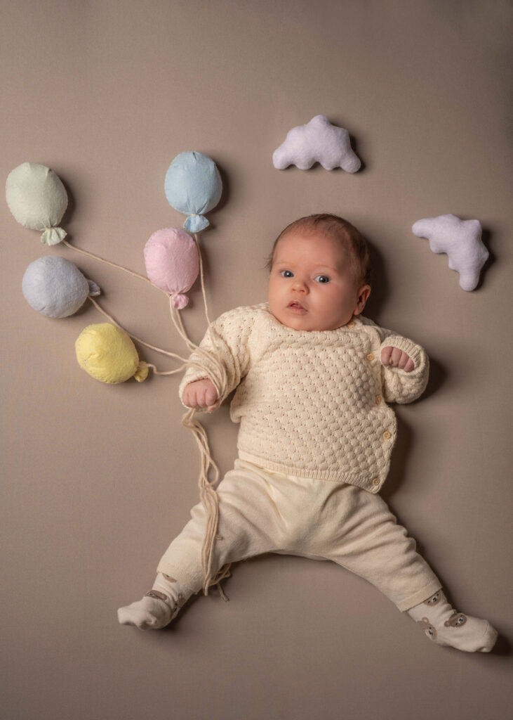 Porträtt av bebis som ligger och håller i ballonger av tyg.