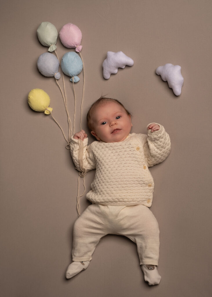 Porträtt av bebis som ligger och håller i ballonger av tyg.