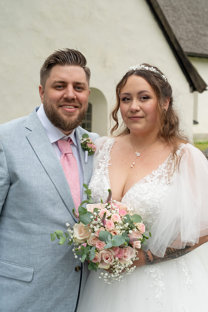 Porträtt på brudparet. Bruden i vacker vit klänning och maken i grå kostym med rosa slips.