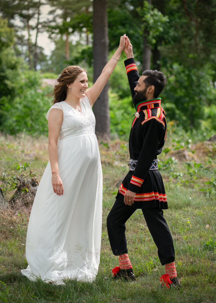 Brudparet tittar på varandra och har armarna upp i luften. De är glada.