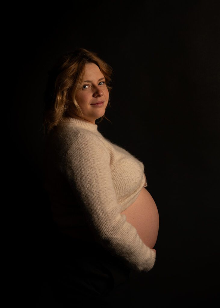 Porträtt av gravid kvinna. Från sidan. Svart bakgrund.