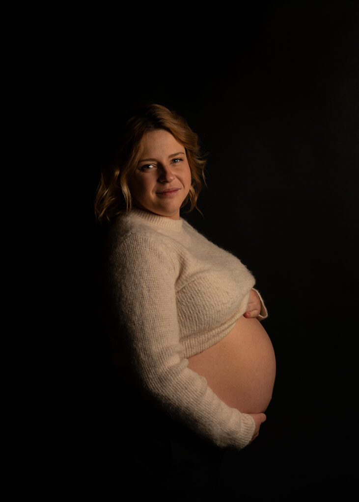 Porträtt av gravid kvinna. Från sidan. Svart bakgrund.