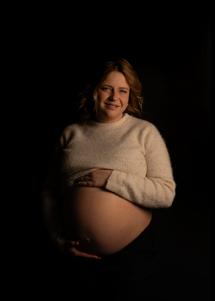 Porträtt av gravid kvinna. Från sidan. Svart bakgrund.